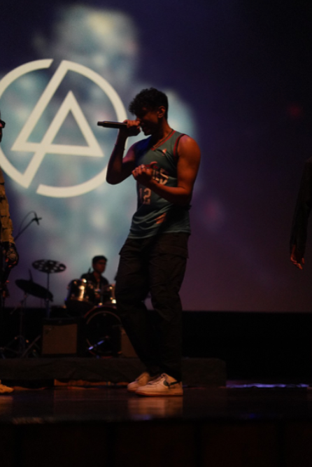 Yash Lothe performing on stage with a microphone at a college concert, a Linkin Park logo projected behind him.